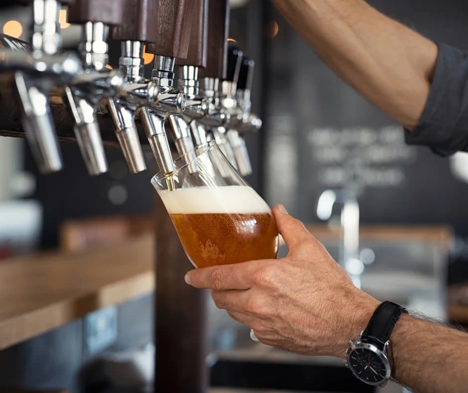 A hand pours beer into a glass from a tap at a bar.
