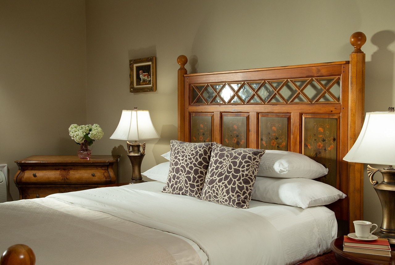 A neatly arranged bedroom featuring a wooden bed with decorative pillows, a nightstand with a lamp, and a vase of flowers.