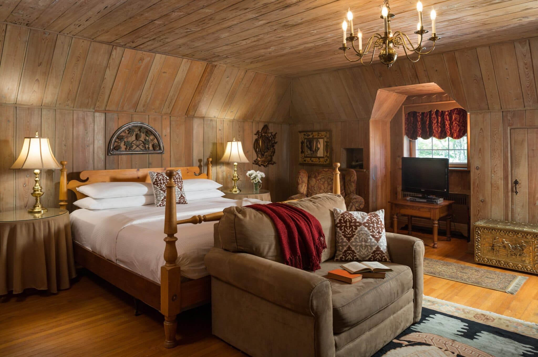 Cozy wooden-paneled bedroom featuring a queen bed, armchair, and decorative lighting.