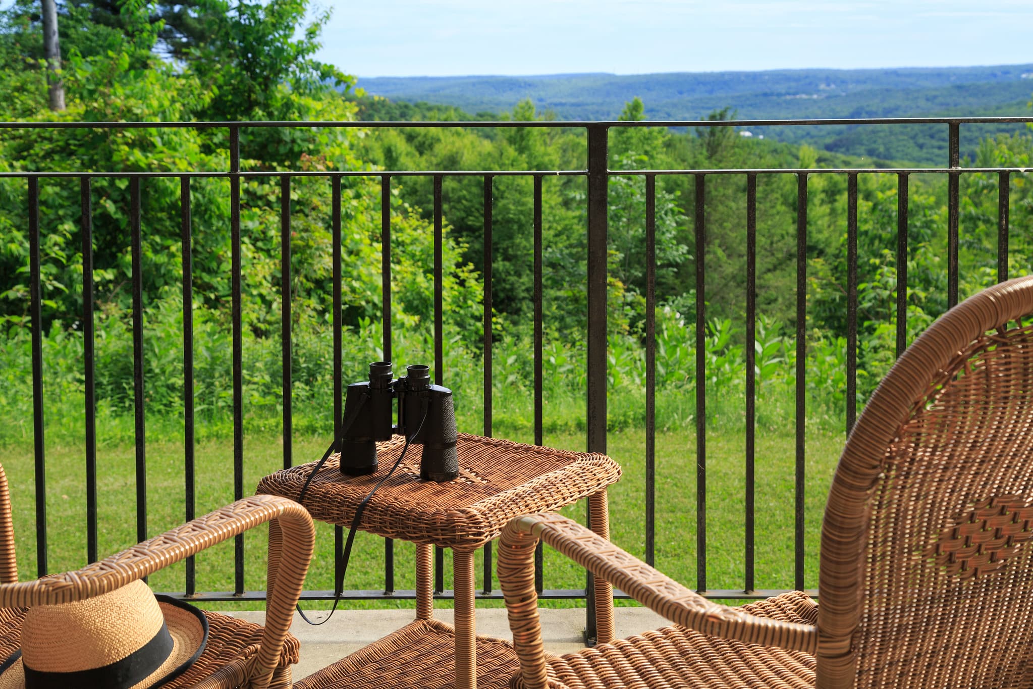 A cozy balcony scene featuring binoculars on a wicker table with green hills in the background.