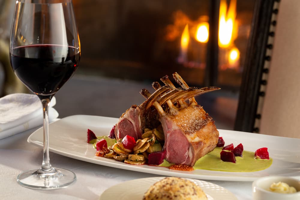 Rack of lamb, red wine in stemmed glass and fireplace glowing in background