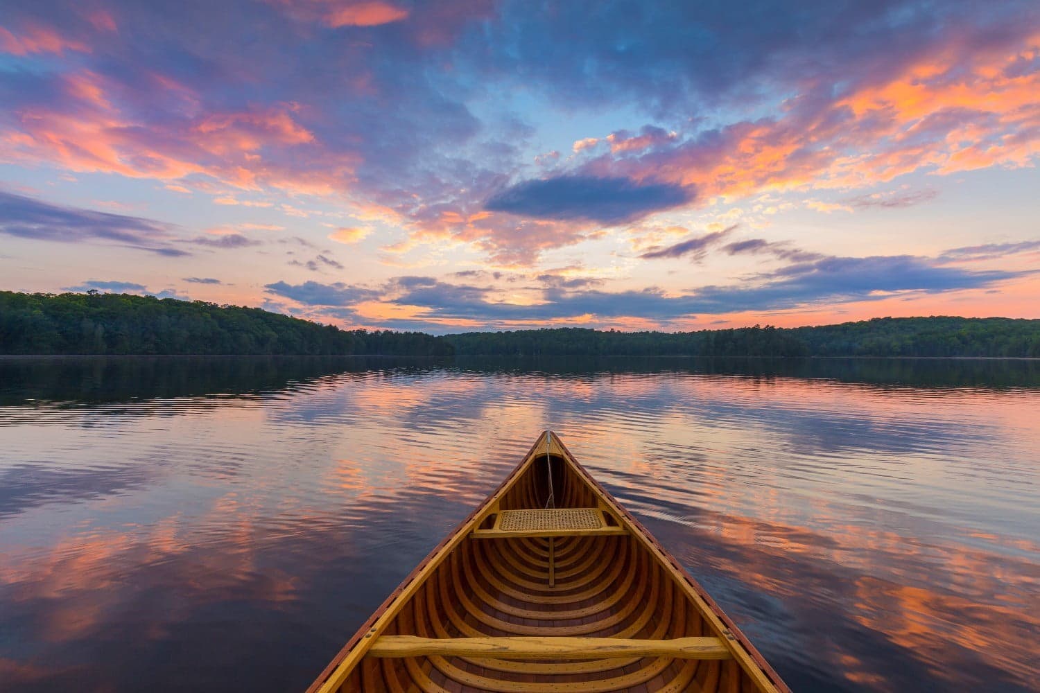 A wooden canoe floats on a calm lake reflecting a colorful sunset. A wooden canoe floats on a calm lake reflecting a colorful sunset.