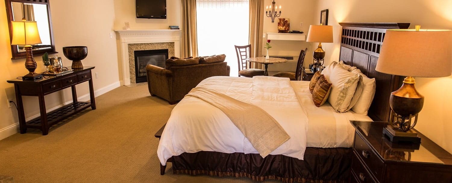 A cozy hotel room featuring a large bed, dresser, seating area, and fireplace.