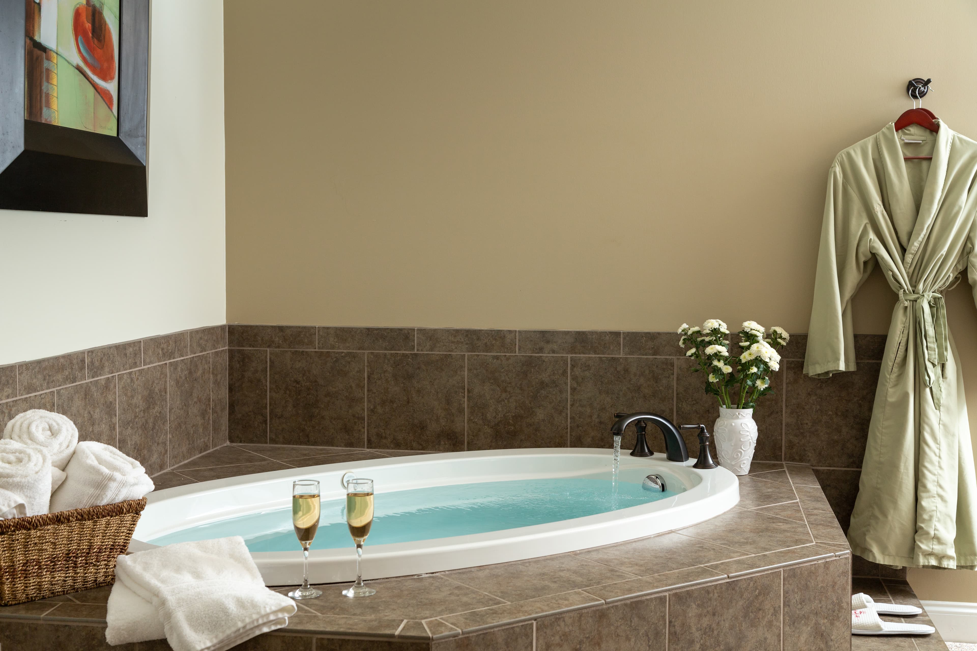 A luxurious bathroom featuring a jetted bathtub, a green robe, fresh flowers, folded towels, and two flutes of champagne.