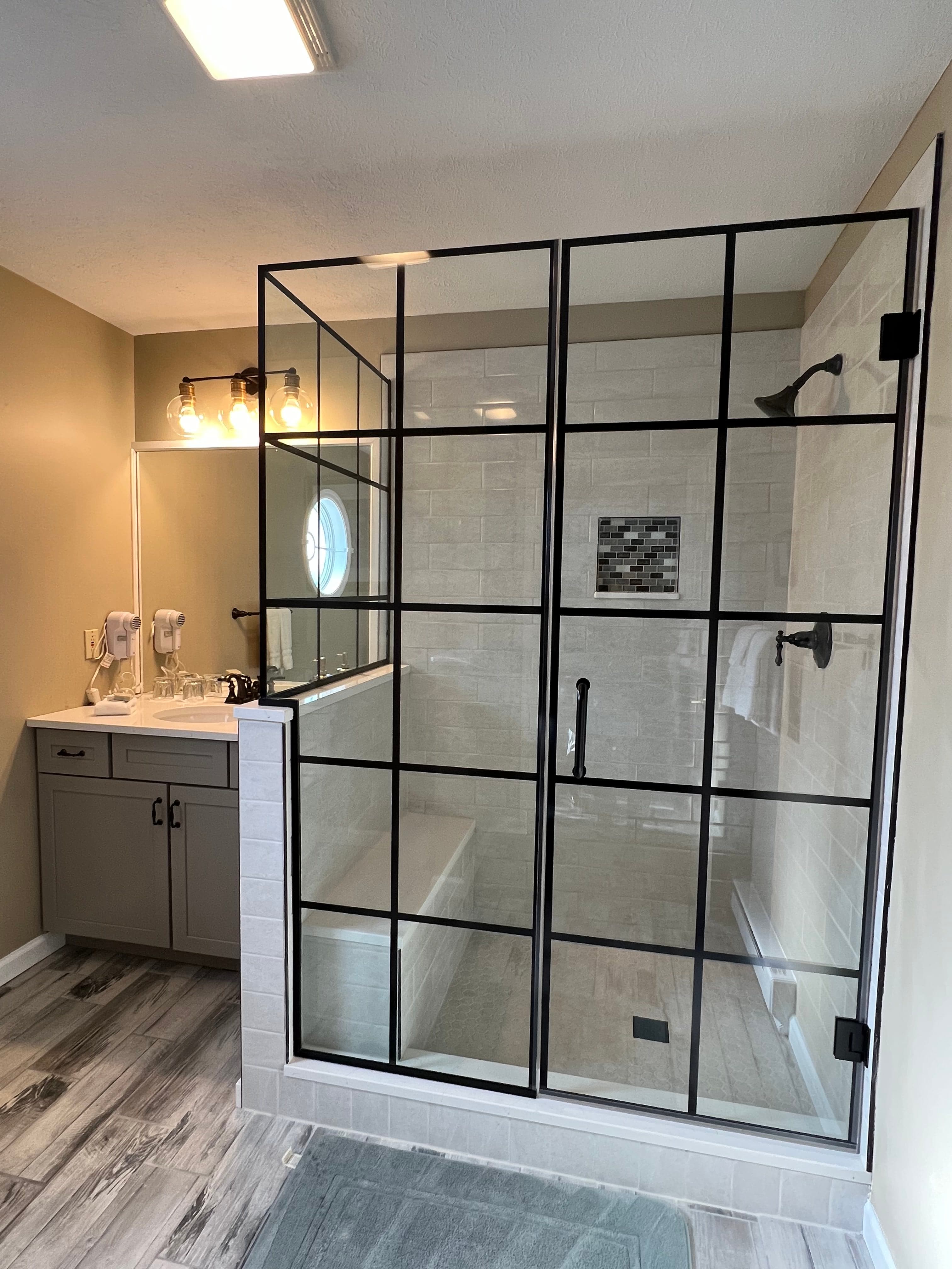 Modern bathroom with a glass shower enclosure, gray vanity, and bright lighting.
