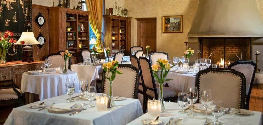 Elegant restaurant interior with white tablecloths, floral centerpieces, and a cozy fireplace.