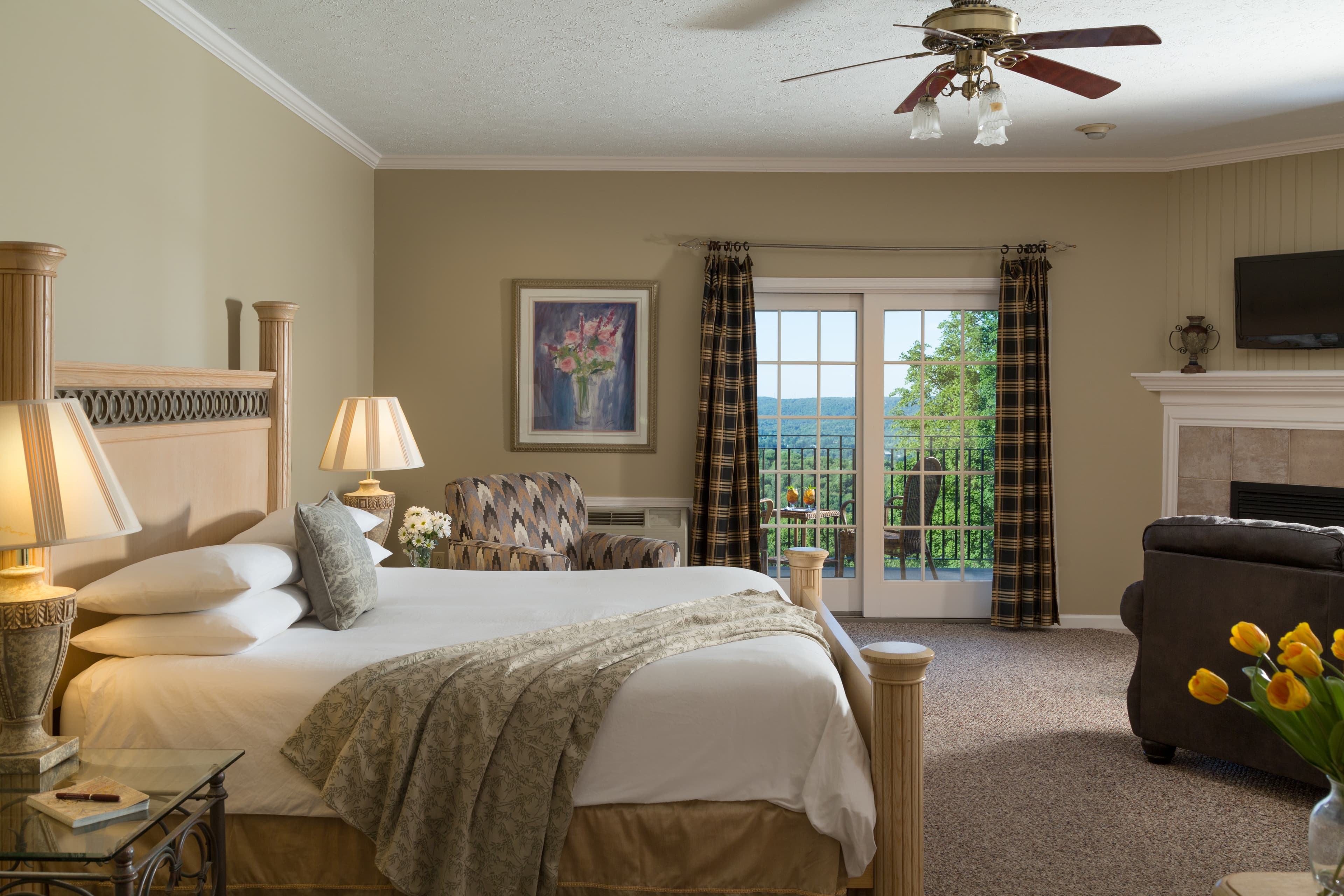 A cozy hotel room featuring a large bed, decorative furniture, and a sliding glass door leading to a scenic balcony.