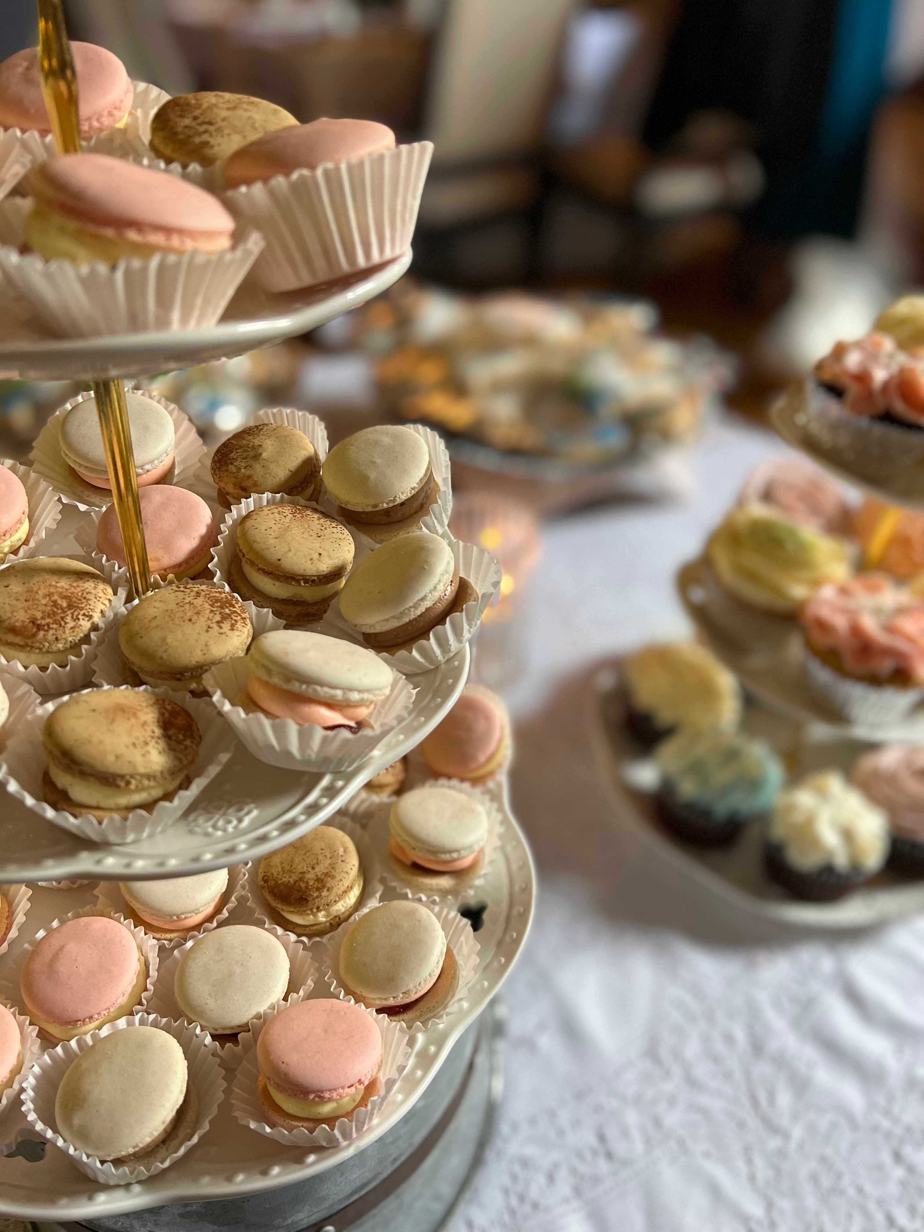 A white tiered stand displaying a variety of macarons in shades of pink and white, with paper liners underneath each.