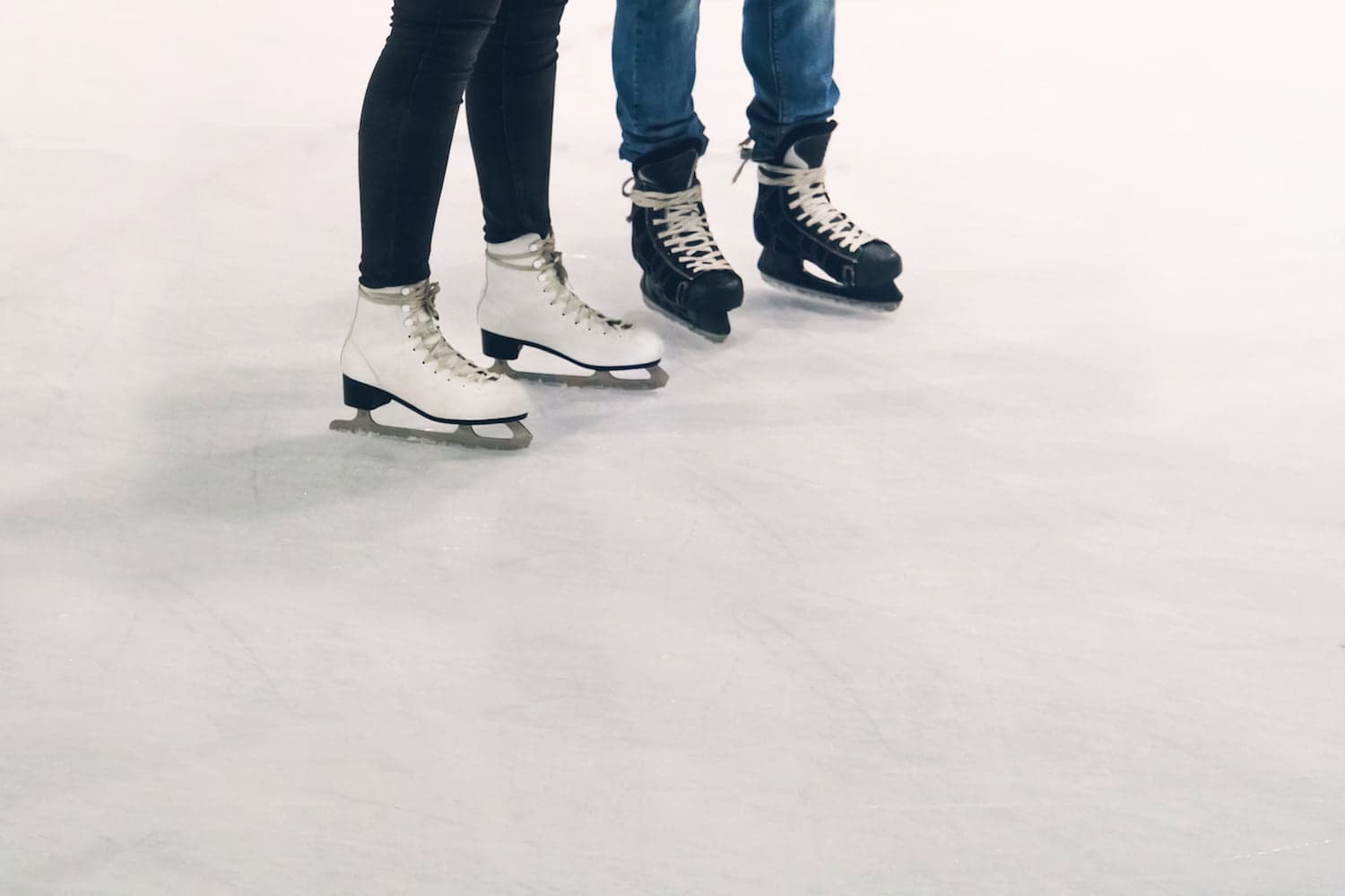 Two pairs of legs in ice skates stand on an ice rink.