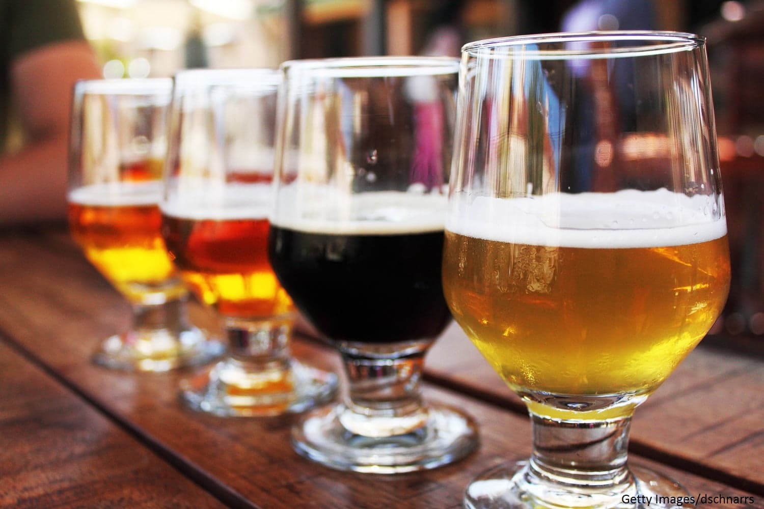 A row of four different styles of beer served in glasses on a wooden table.