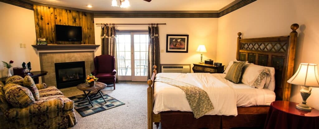 Cozy bedroom with a wooden bed, seating area, fireplace, and patio doors.