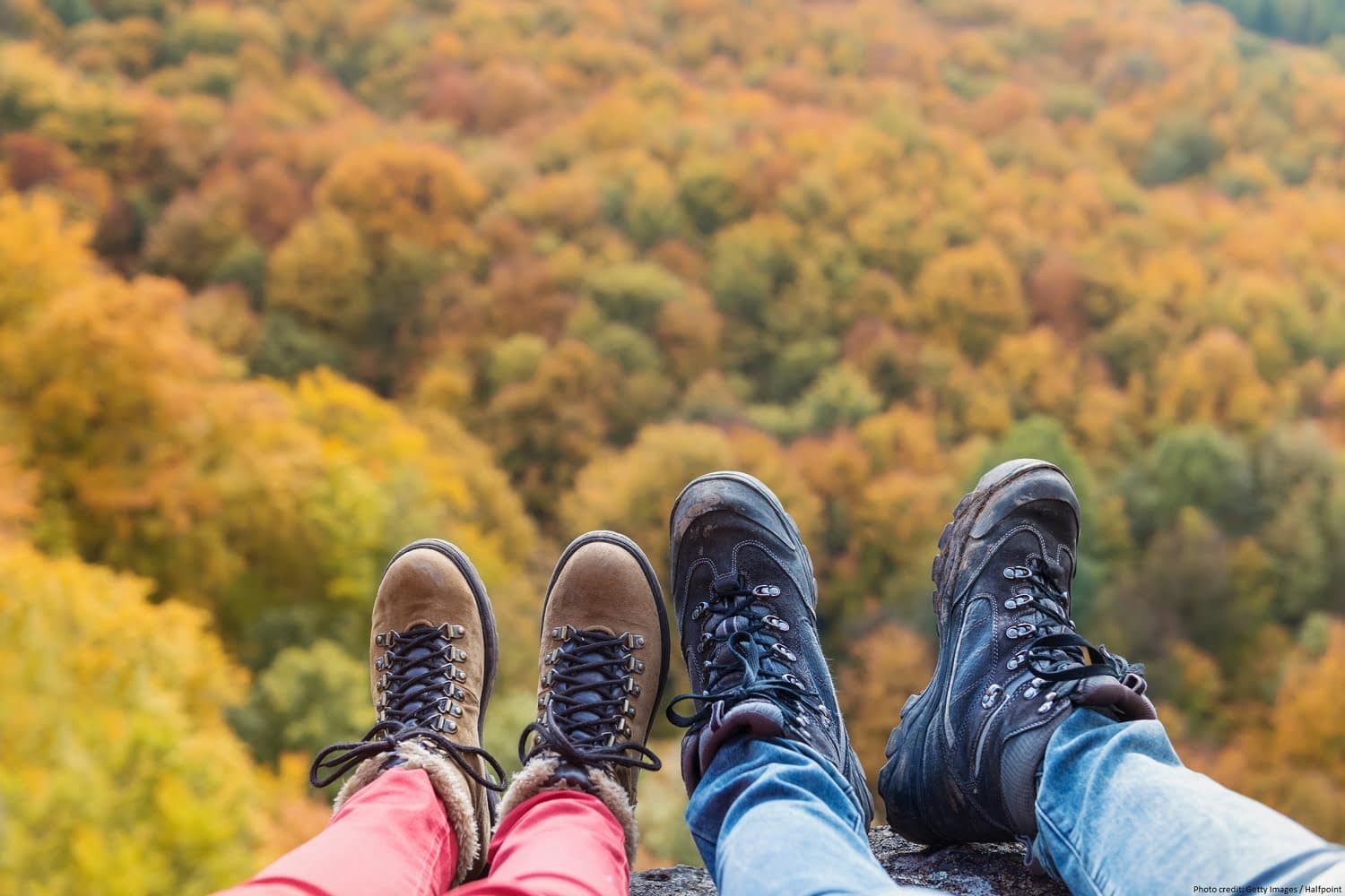 A pair of hiking boots and outdoor shoes resting on the edge of a cliff, overlooking a colorful autumn forest.