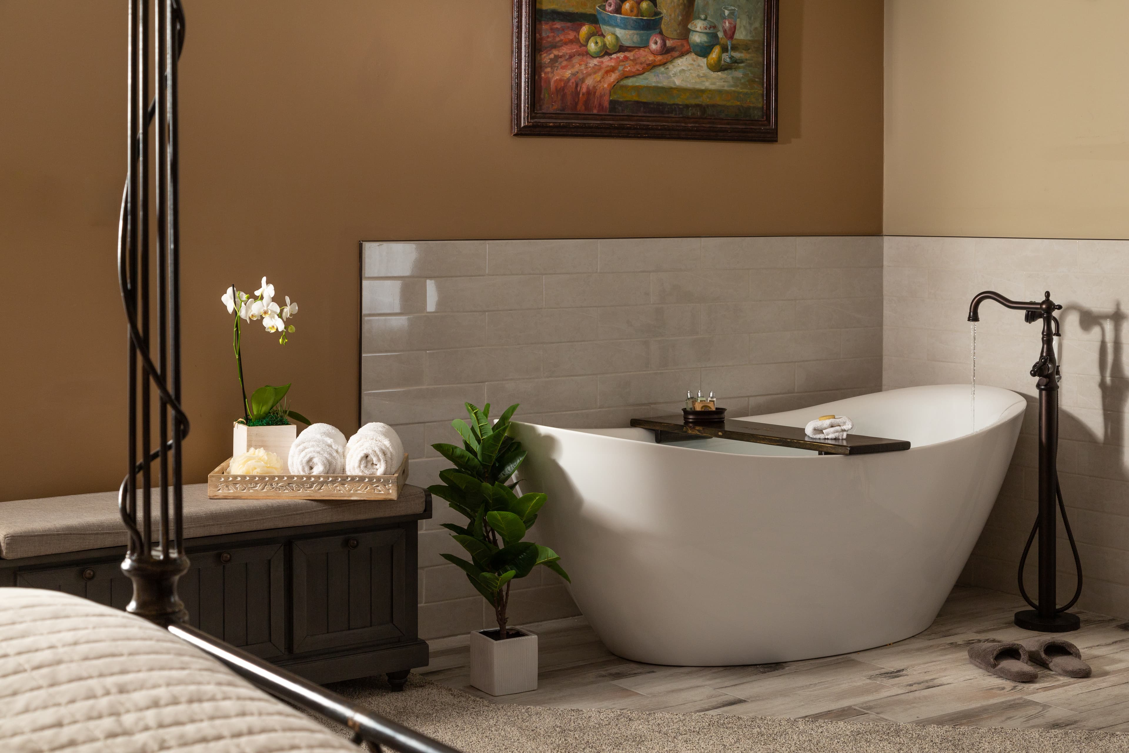 A modern bathroom featuring a freestanding bathtub, decorative plants, towels, and a painting.