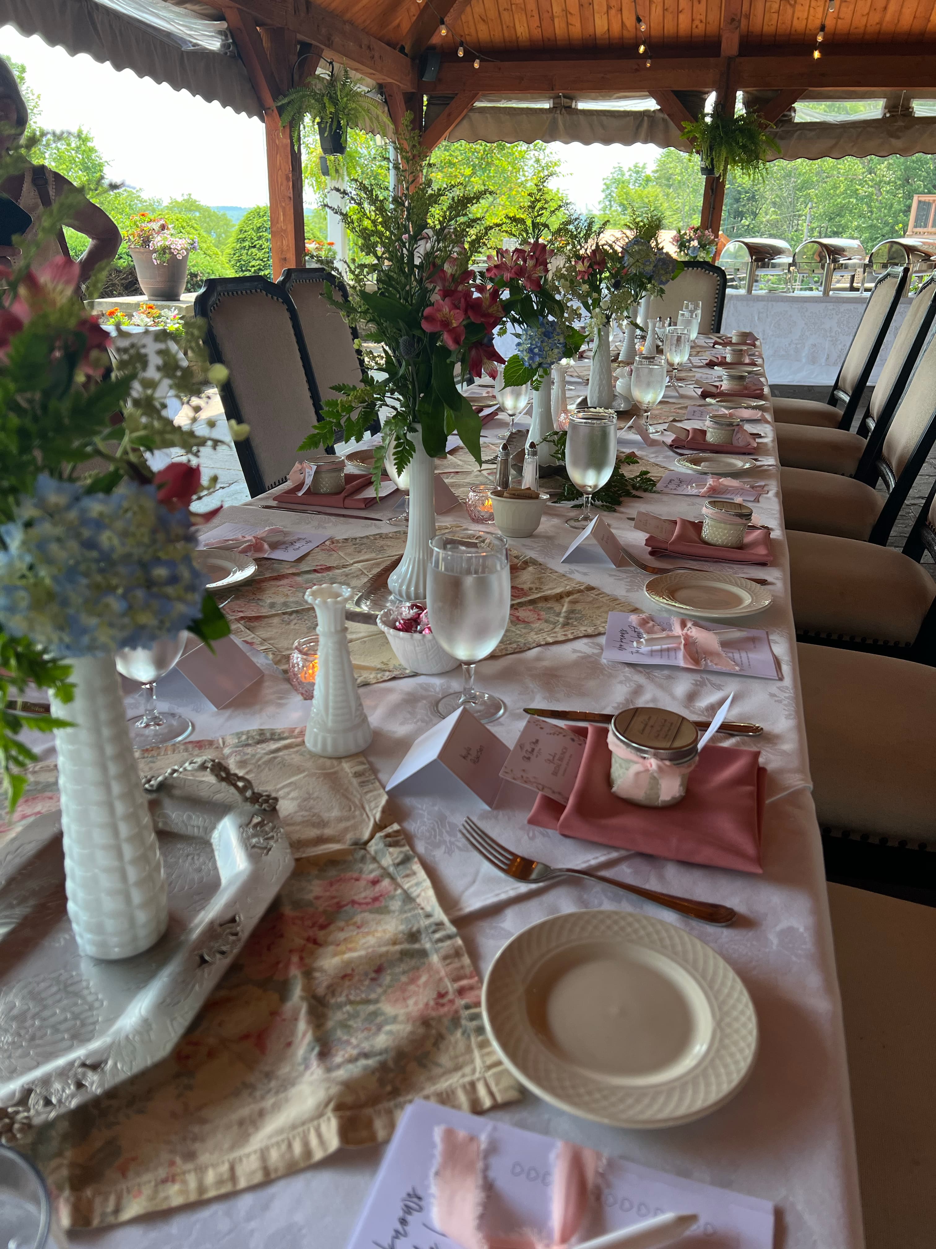 A long table set for a bridal brunch or shower, with floral centerpieces, place settings, and a beautiful view.