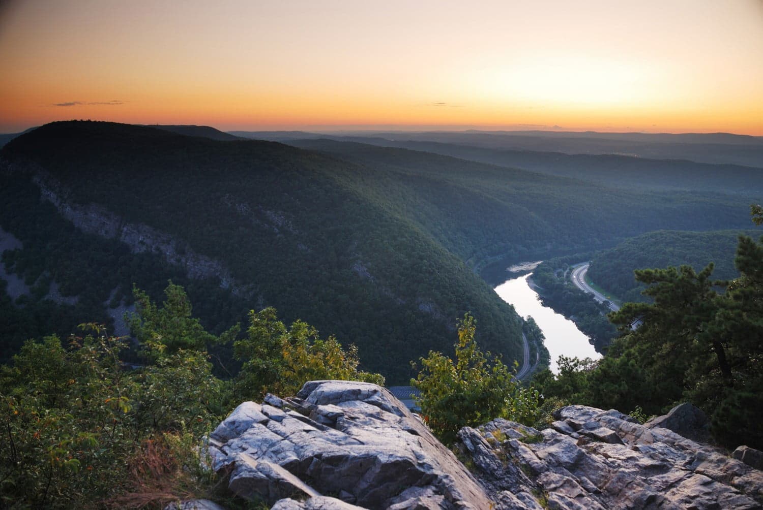 A panoramic view of a river winding through lush valleys at sunset.