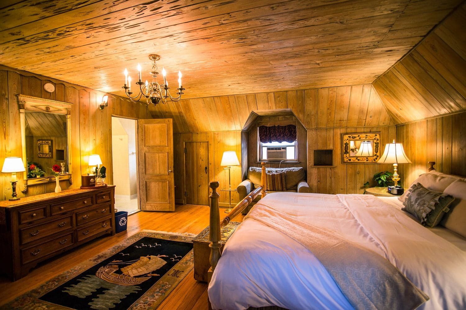 Cozy wooden-bedroom featuring a bed, dresser, lamps, and chandelier.