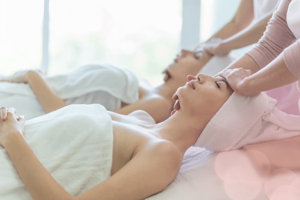 Two women laying on a table covered in a towel with their eyes closed getting massages.