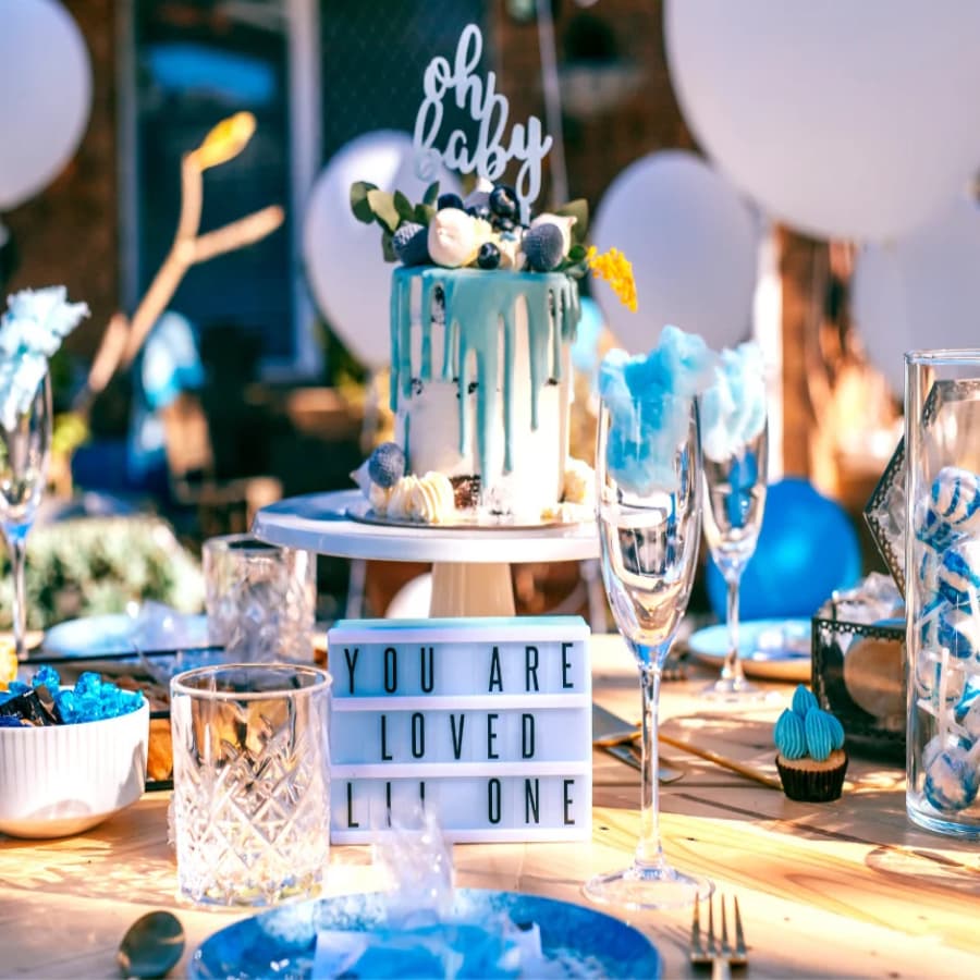 A beautifully decorated baby shower table with a blue and white cake, a "You Are Loved" sign, and blue balloons in the background.