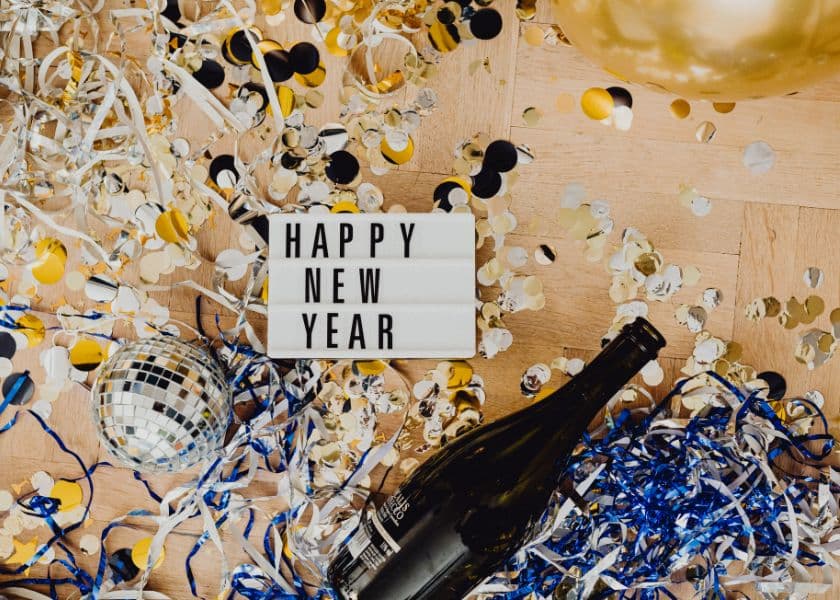 A festive arrangement of confetti, a disco ball, and a champagne bottle with a sign that reads "HAPPY NEW YEAR." A festive arrangement of confetti, a disco ball, and a champagne bottle with a sign that reads "HAPPY NEW YEAR."