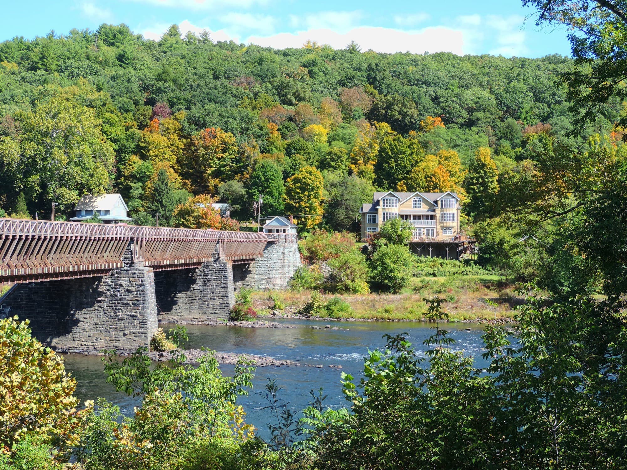 Scenic view of a river with a wooden bridge and a house surrounded by colorful autumn foliage.