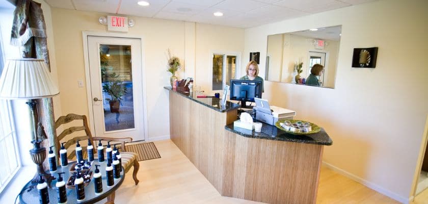A reception area with a wooden desk, a seated attendant, and a display of products on the counter.