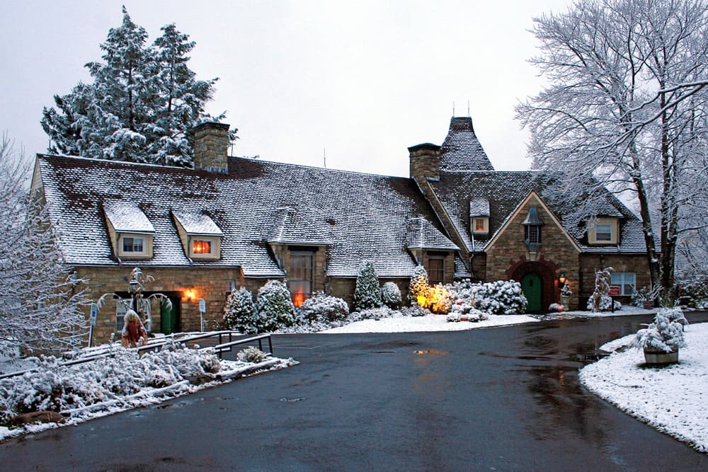 A picturesque winter scene of the French Manor Inn and Spa, with snow-covered trees and lights illuminating the entrance.
