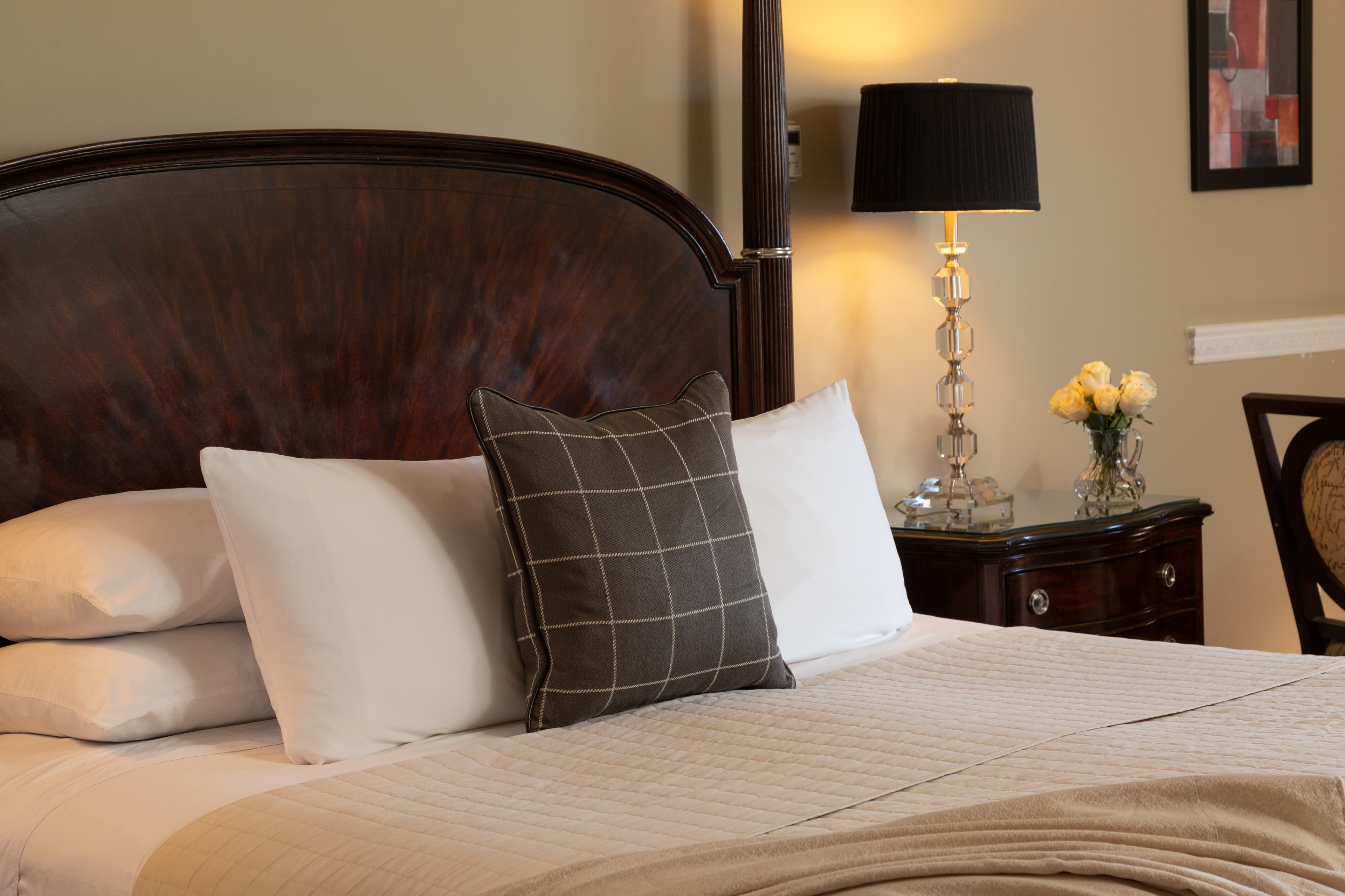 A neatly made bed featuring decorative pillows, a stylish lamp, and a vase of yellow flowers.
