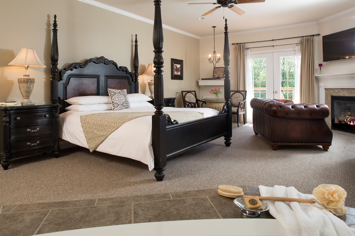 A serene hotel room featuring a four-poster bed, a cozy leather sofa, and a fireplace.