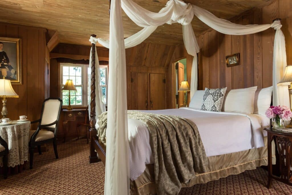 Cozy bedroom with wooden walls, a canopied bed, and a small seating area.