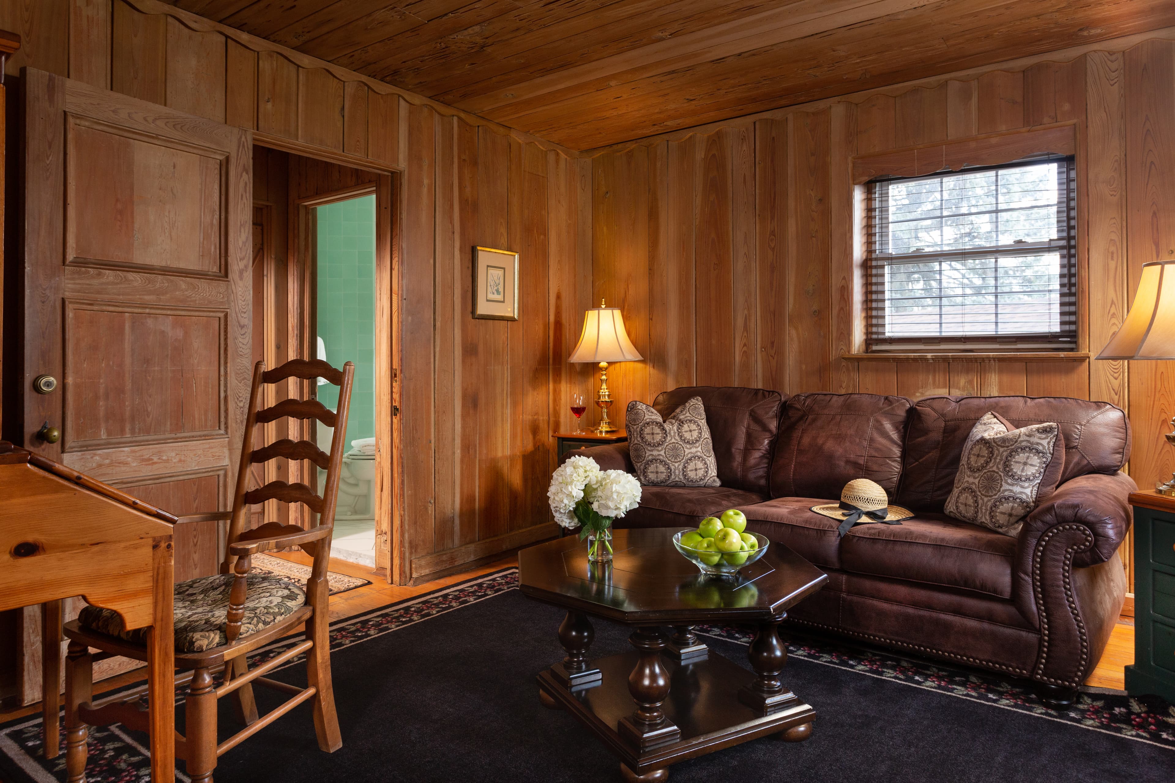 Cozy living room with wooden walls, a brown sofa, a coffee table, and a chair, featuring warm lighting and decorative elements.