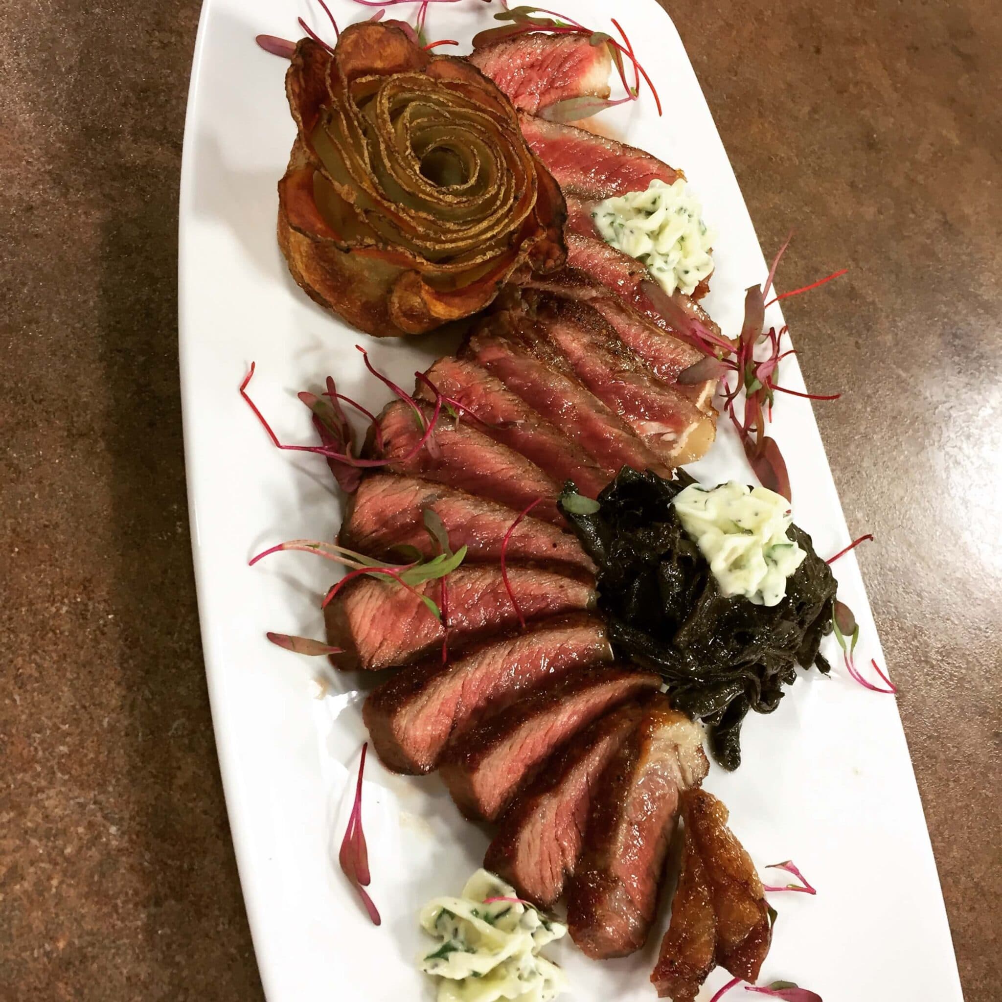 A plate of sliced steak garnished with herbs, accompanied by a roasted onion and sauces.