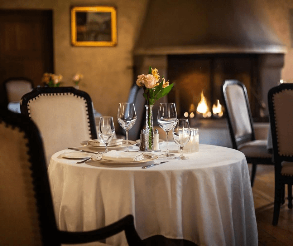 A beautifully set dining table with elegant glassware and a floral centerpiece, next to a cozy fireplace.