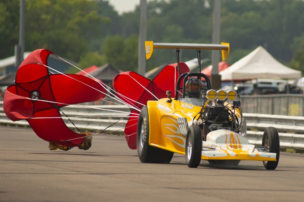 A yellow drag racing car slowing down with its parachute deployed.