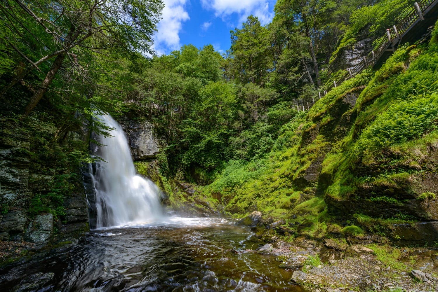 A cascading waterfall surrounded by lush greenery and blue skies.