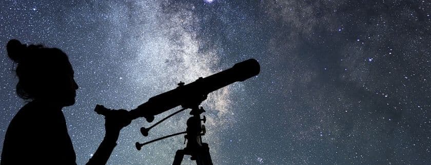 A silhouette of a person using a telescope under a starry night sky.