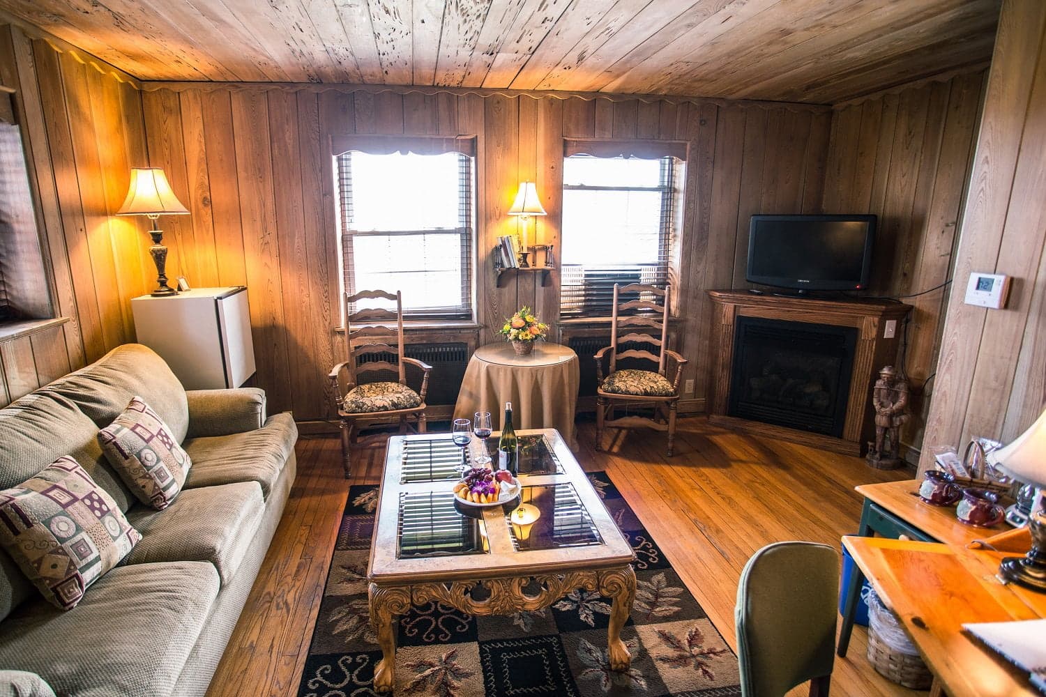 A cozy living room featuring wooden walls, a sofa, two chairs, a coffee table, and a TV.