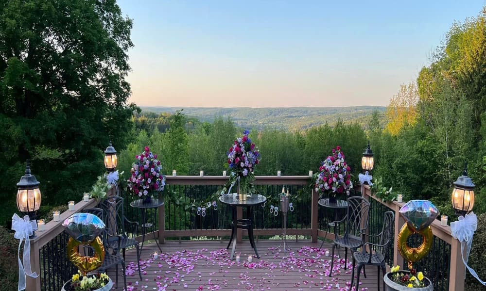 A romantic outdoor proposal setup with a flower arrangement, candles, and a scenic view of the Poconos mountains.