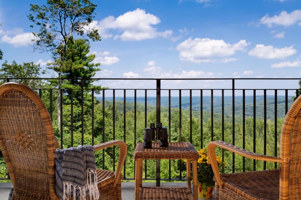 A serene balcony with wicker chairs overlooking a lush green landscape and blue sky.