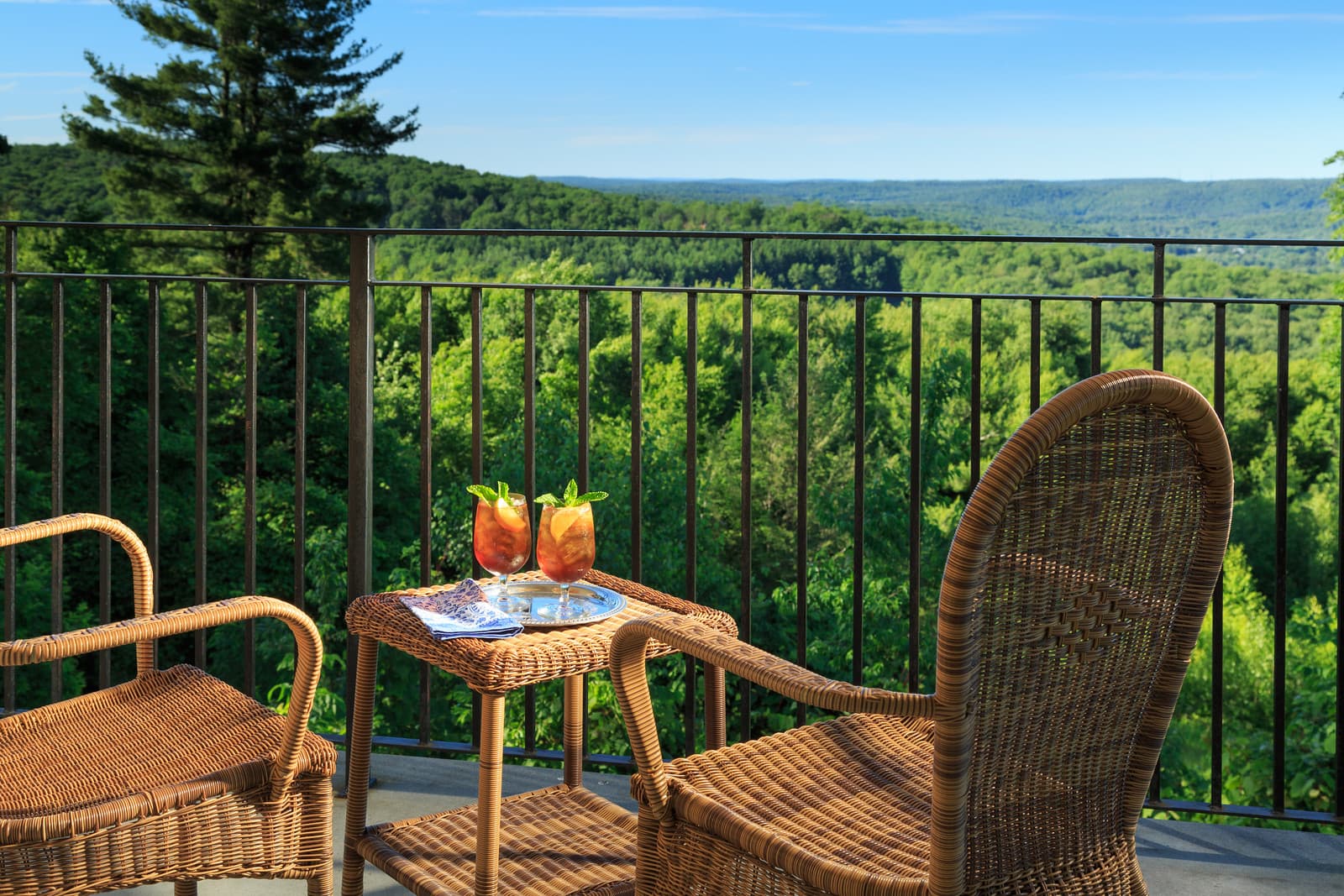 Two cocktails on a table between wicker chairs overlooking a lush green landscape.