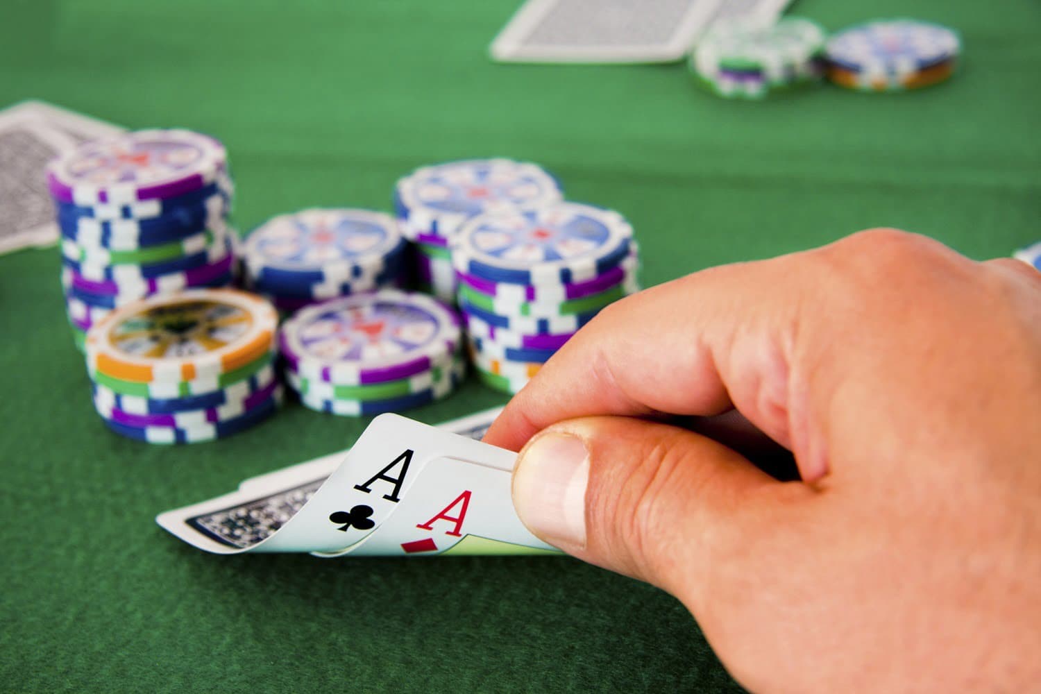 A hand holds two aces over a pile of poker chips on a green table.