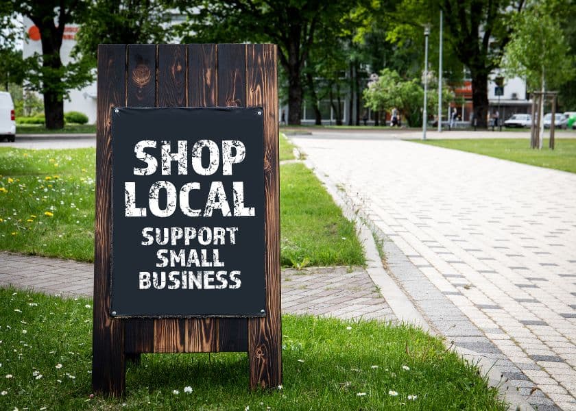A wooden sign in a park encourages people to "Shop Local" and "Support Small Business." A wooden sign in a park encourages people to "Shop Local" and "Support Small Business."