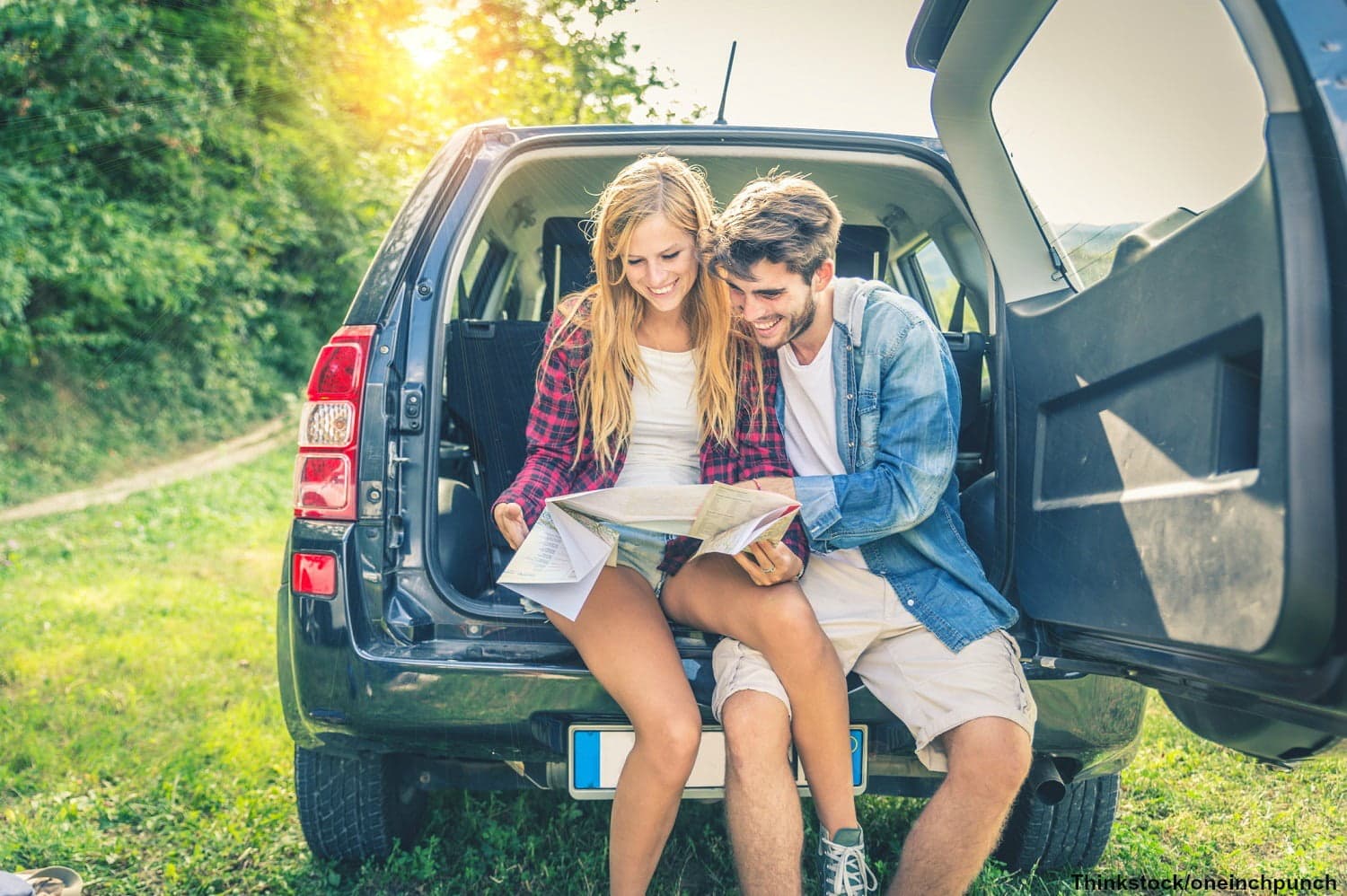 A young couple sits in the back of a car, examining a map in a scenic outdoor setting.