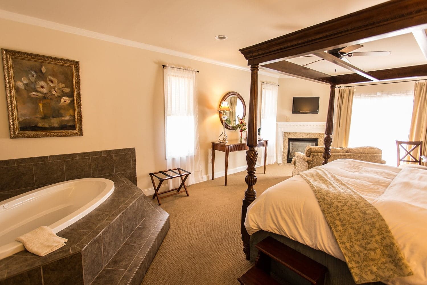 A cozy bedroom featuring a four-poster bed, a modern bathtub, and a sitting area.