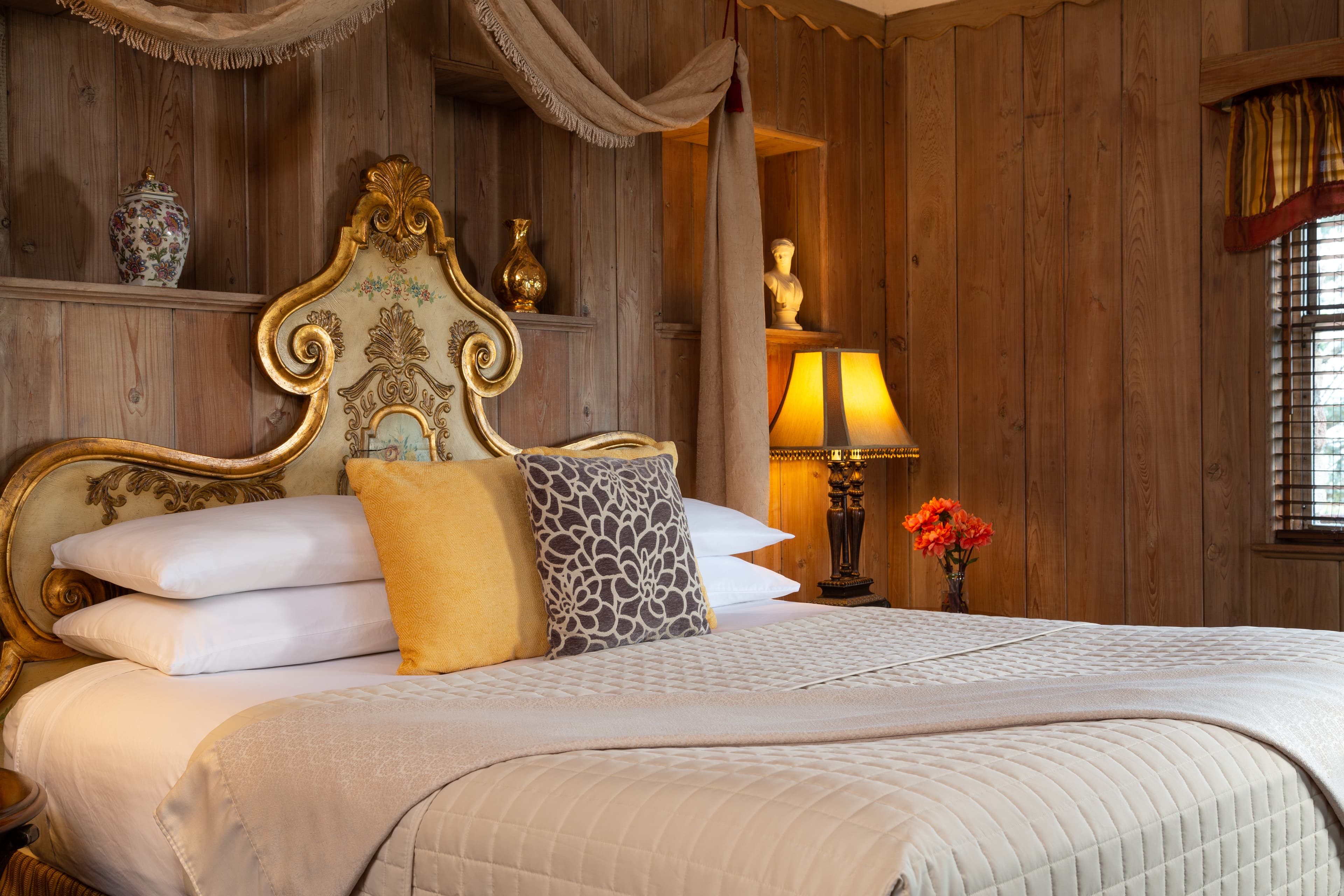 A luxurious bed with an ornate headboard, decorative pillows, and warm lighting in a cozy wooden room.