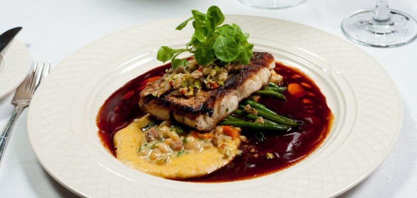 Grilled fish fillet on a bed of green beans, garnished with herbs and served with a rich sauce.