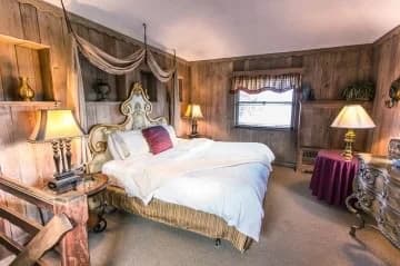 Cozy bedroom featuring a large bed, wooden panel walls, and soft lighting from bedside lamps.
