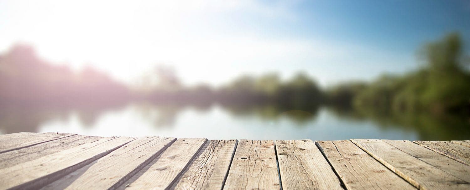 A wooden dock or platform extending into a blurred body of water with a bright sky above.