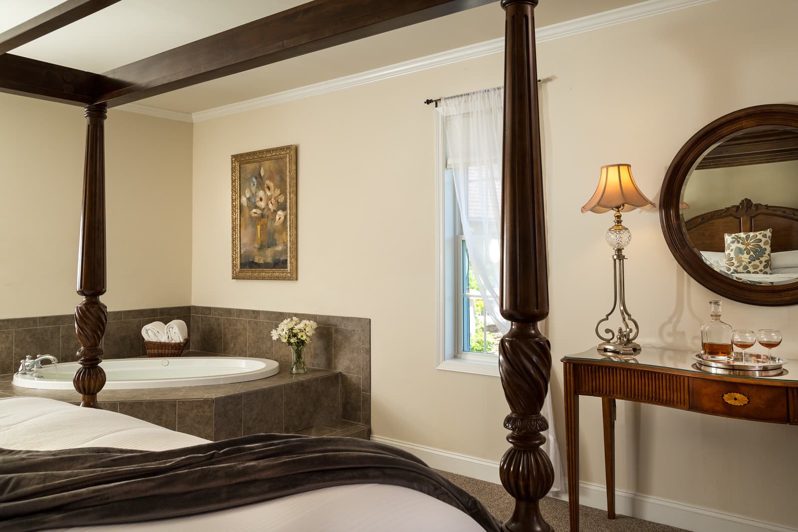 A cozy bedroom featuring a four-poster bed, an elegant mirror, and a relaxing bathtub area.