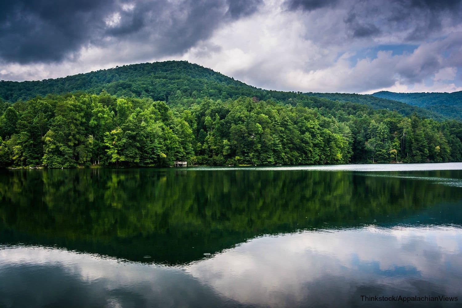 A tranquil lake reflects green hills and an overcast sky. A tranquil lake reflects green hills and an overcast sky.