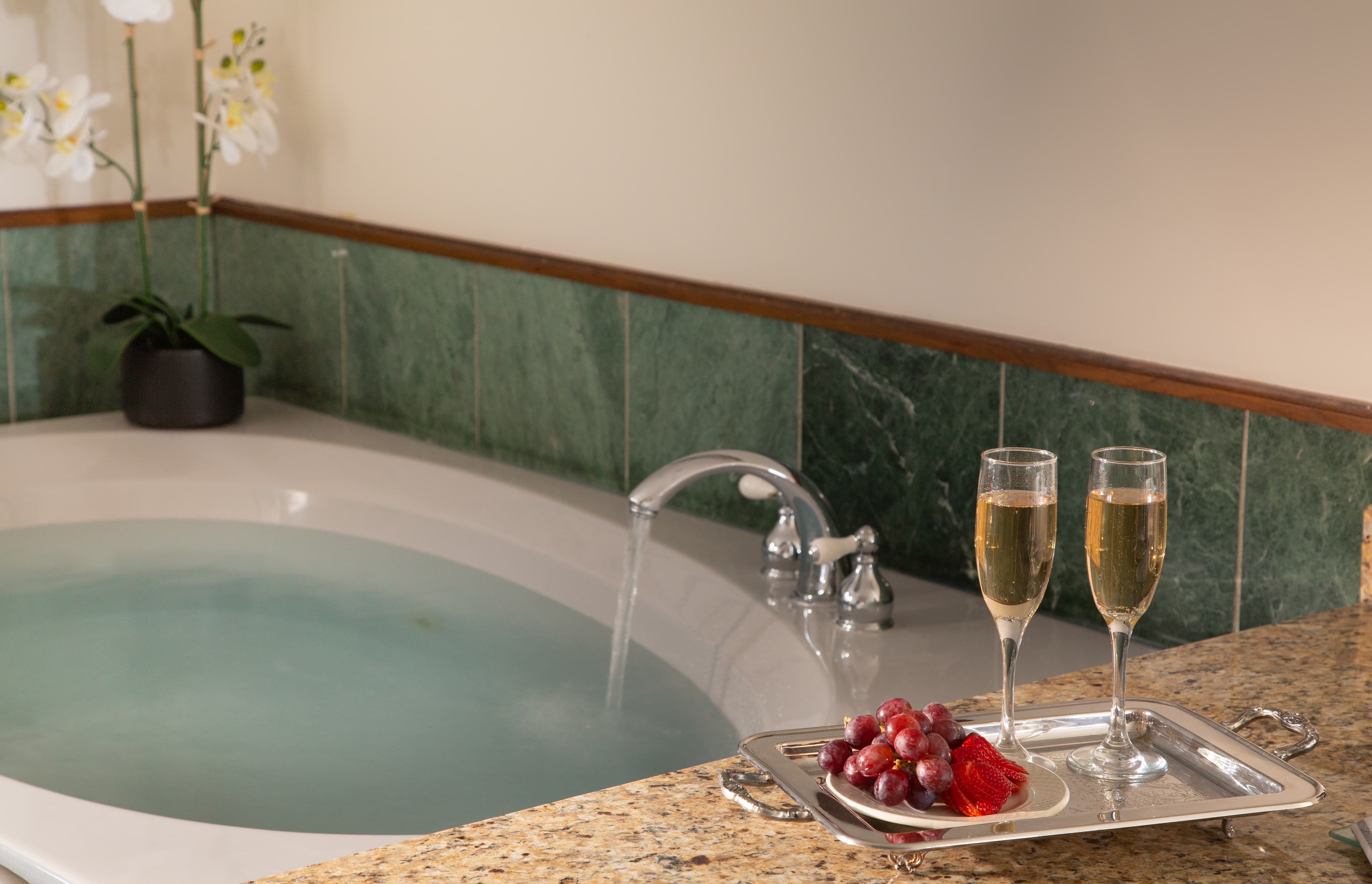 A luxurious bathroom with a soaking tub, two glasses of champagne, and a tray of grapes and strawberries.